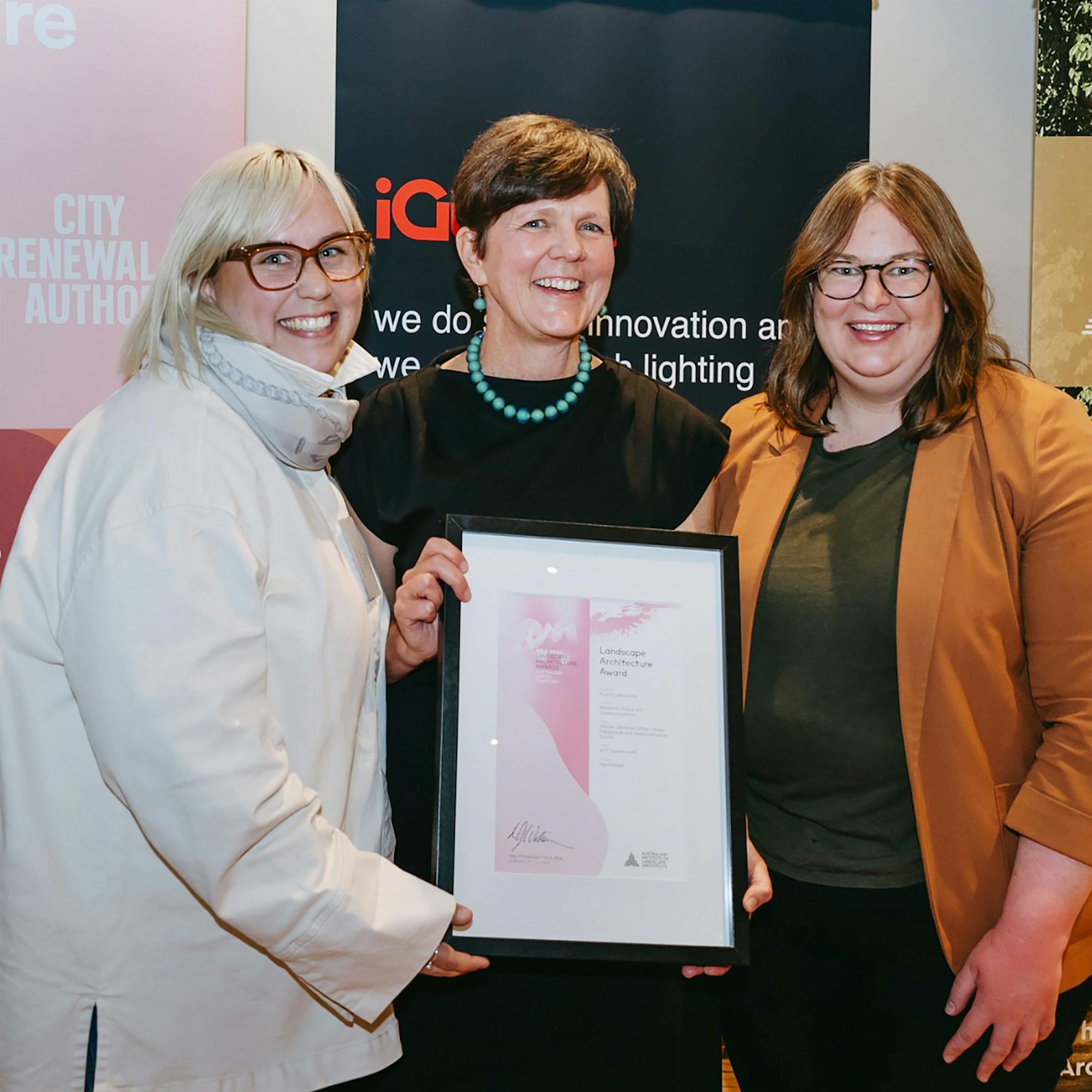 A photo of three people smiling while holding a framed certificate.