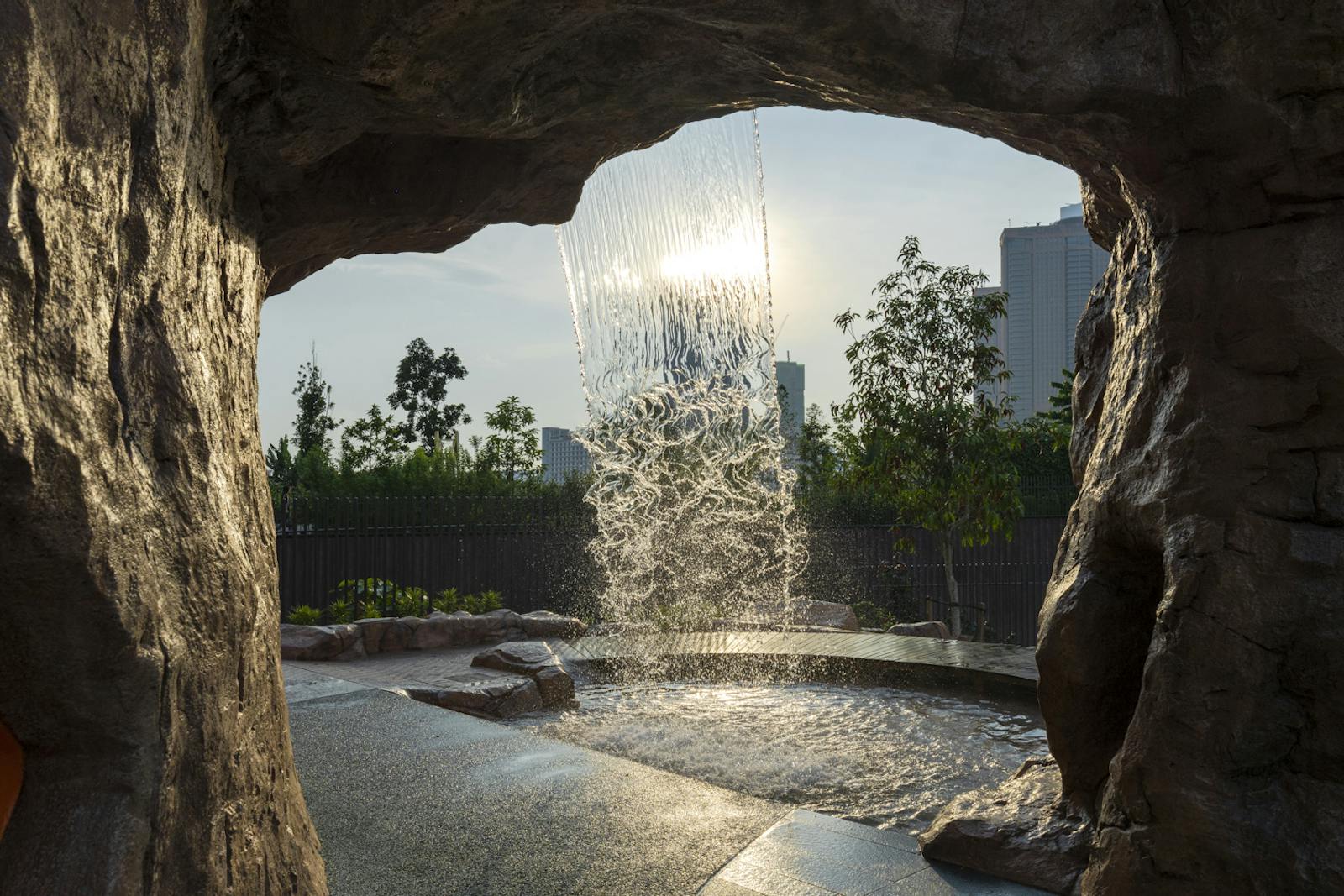 A photo of cascading water taken from inside a cave. Sun and trees are behind.