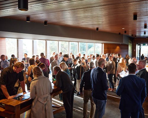 A photo of a large group of people gathering beside large windows in an event space. 