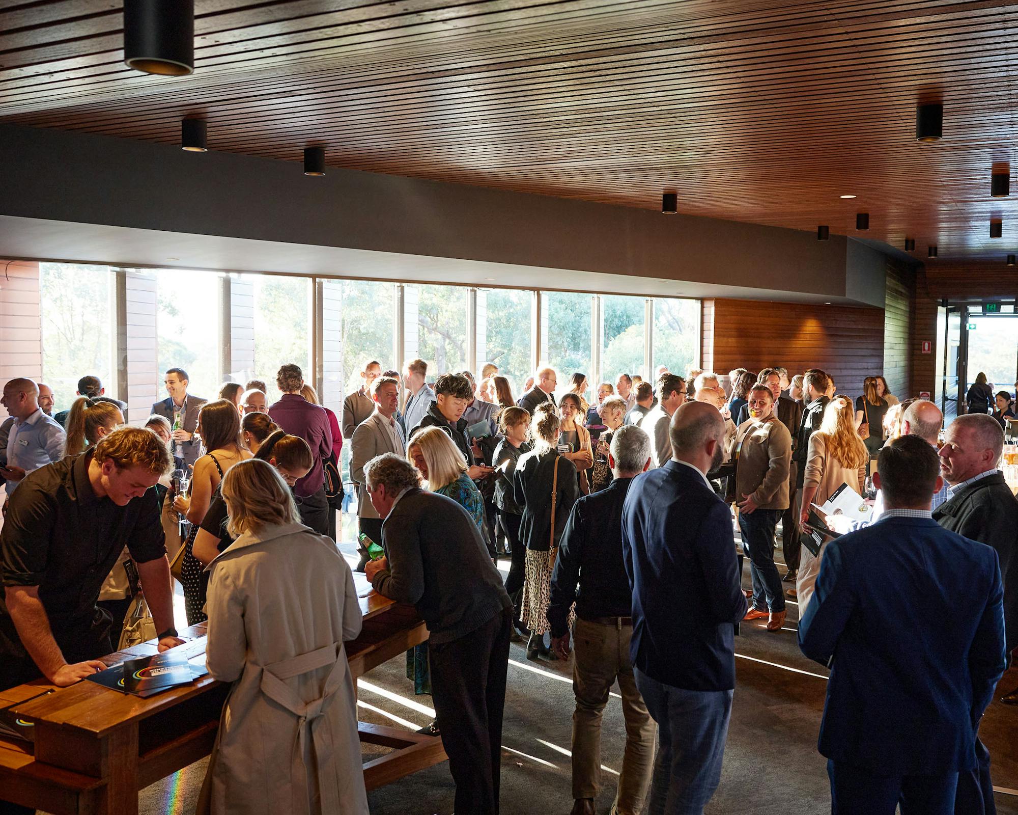 A photo of a large group of people gathering beside large windows in an event space.