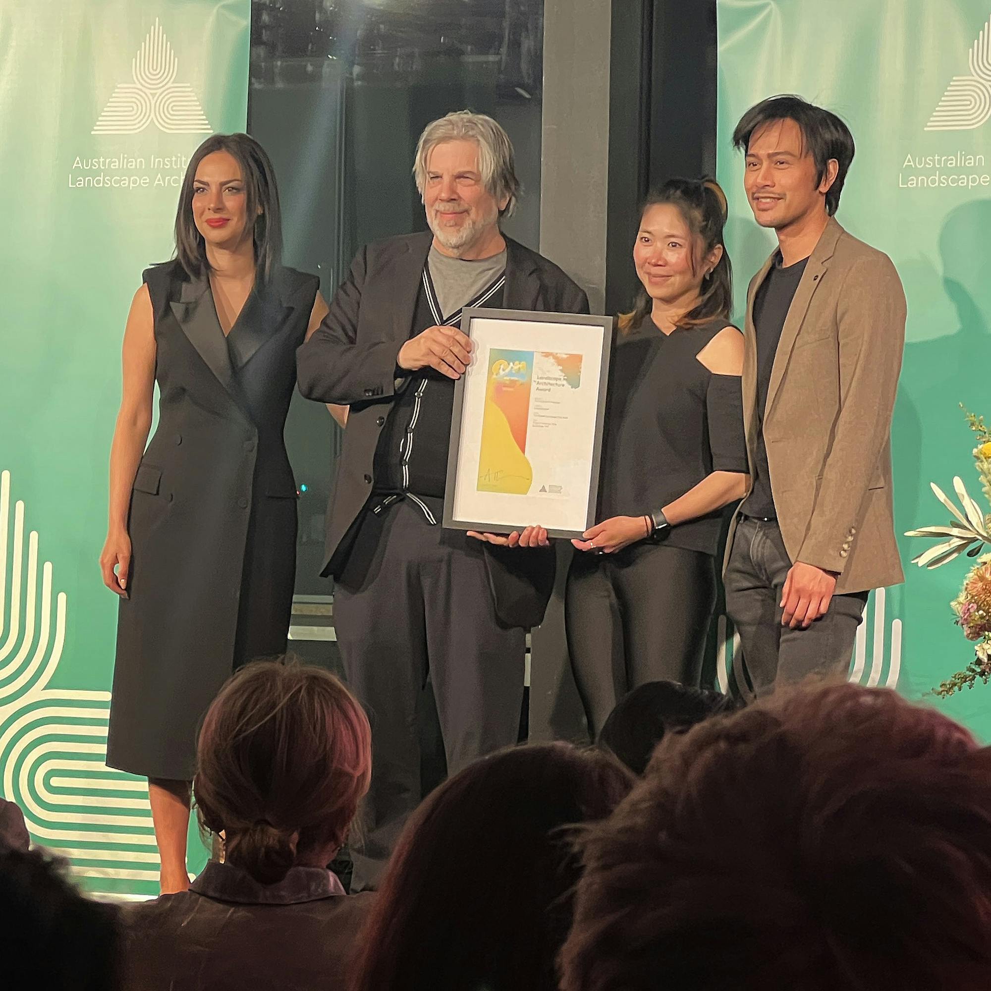 A photograph of four people on stage accepting a framed certificate.