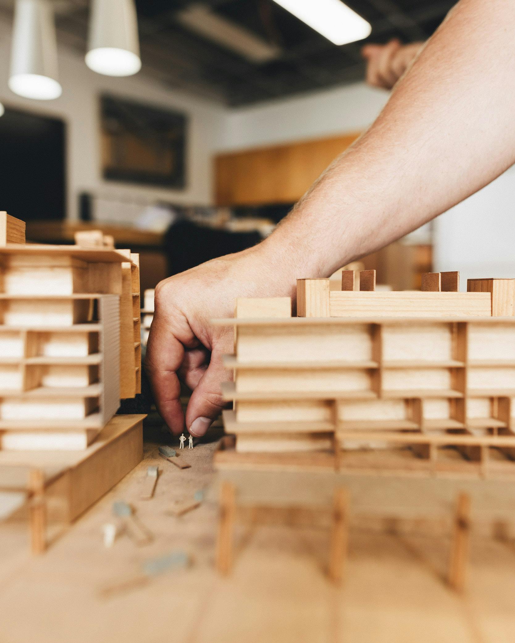 A photograph of a hand moving two small figures within a large timber architectural model.