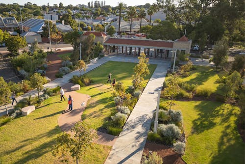 An aerial photograph of a handful of people walking around a park with paved paths, lawn area, and Australian native plants.