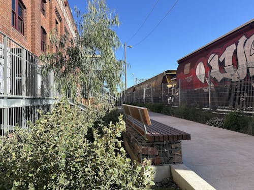 A photograph of pathways, planting, and seating between an old industrial building and railway line.