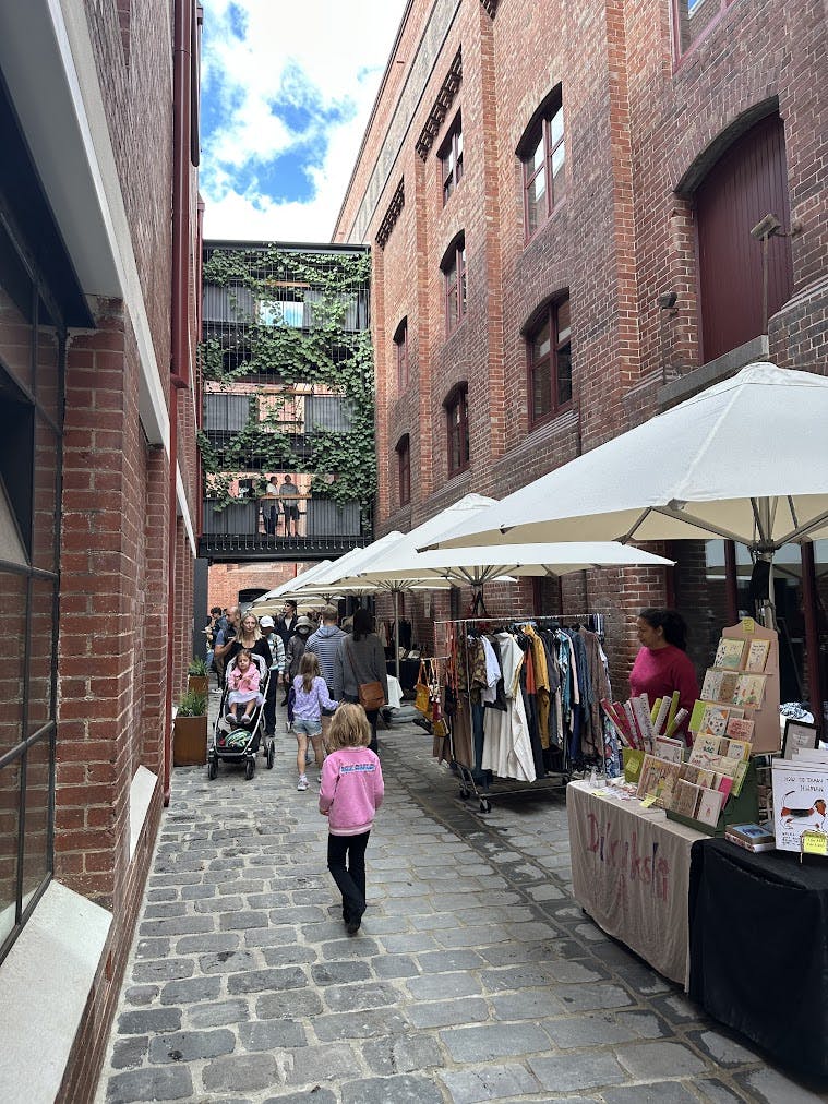 A photo of a restored heritage laneway with a pop up market and greenery growing on pedestrian bridges above.