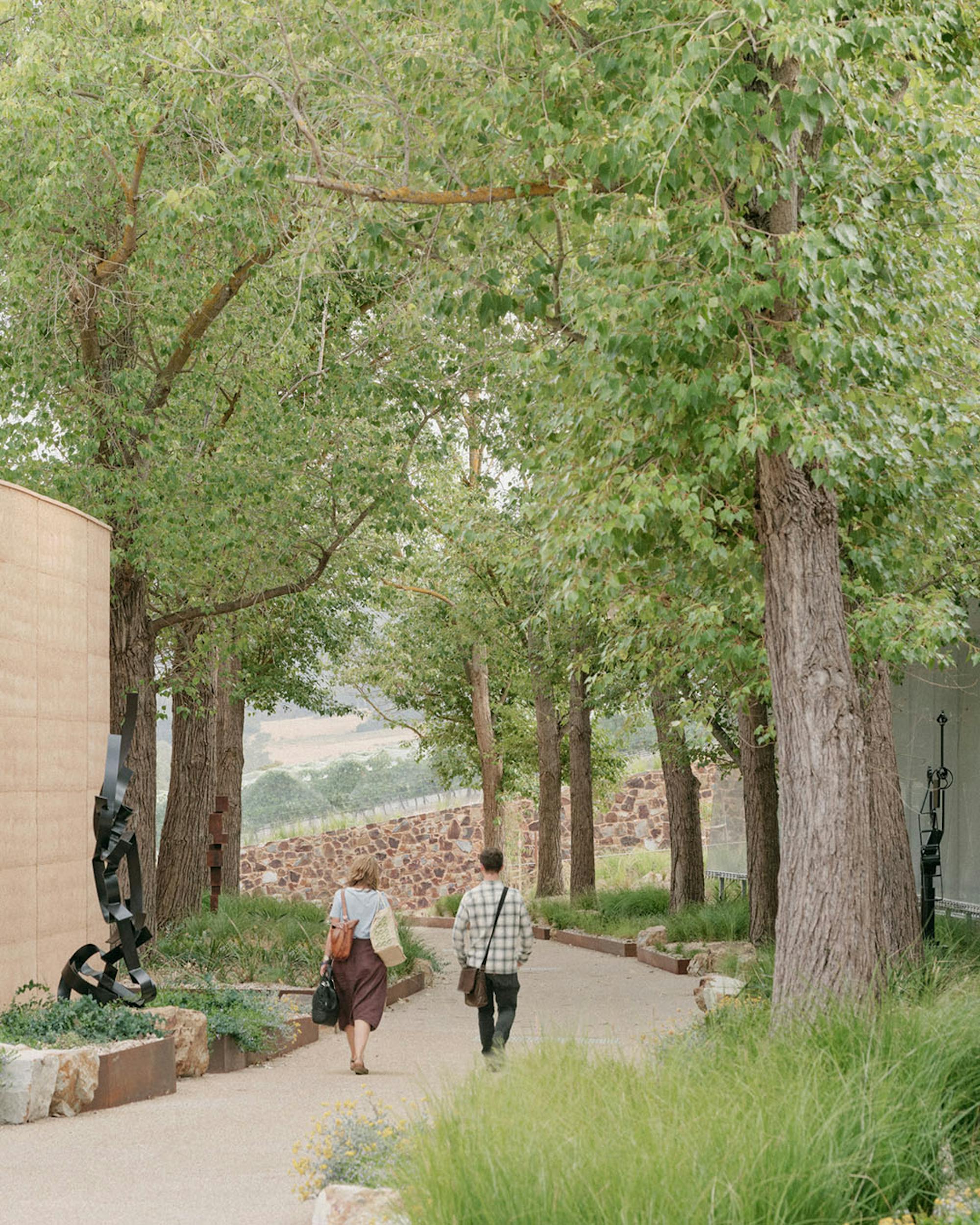 A photo of two people walking on a tree lined lane between two buildings. 