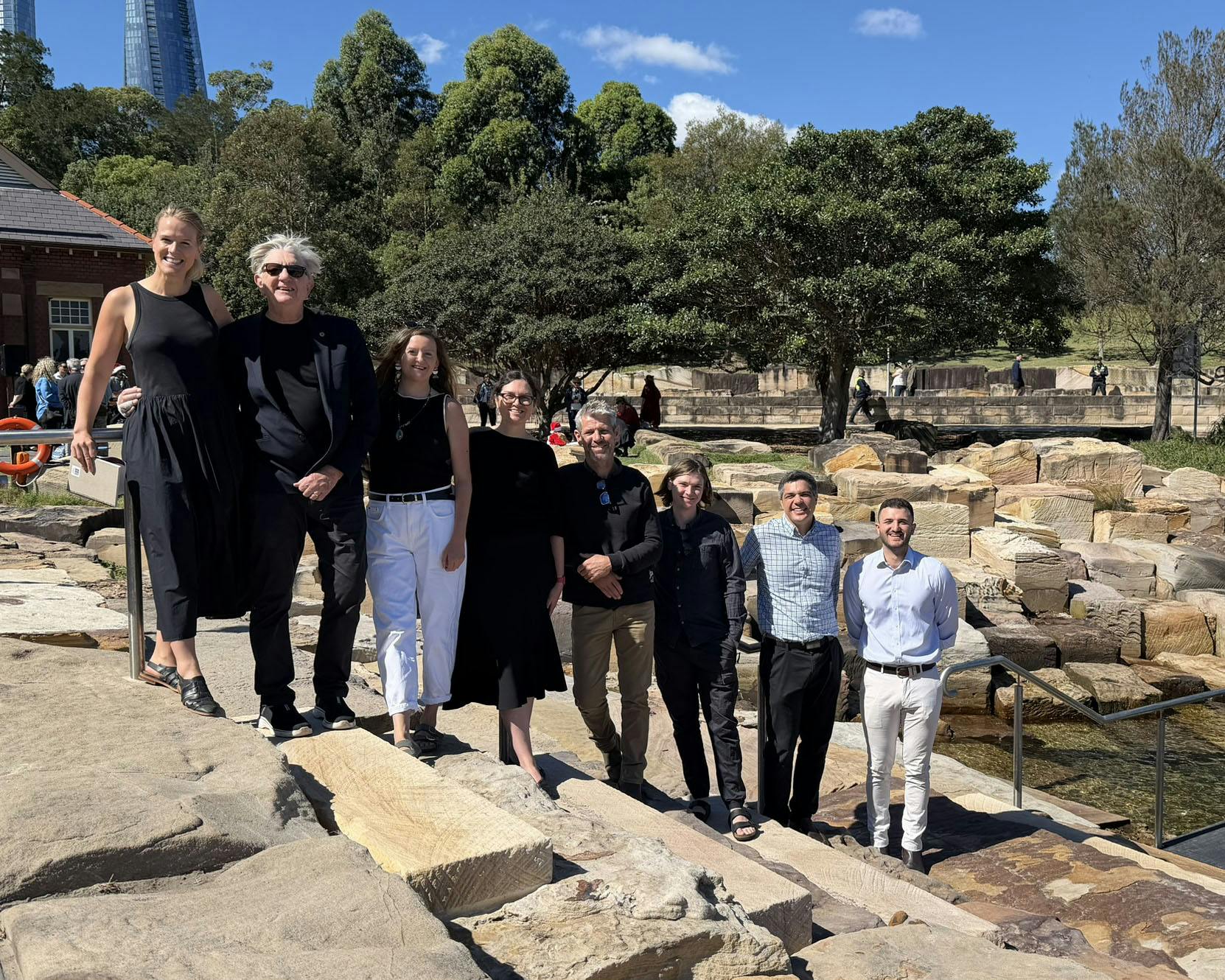 A photo of seven smiling people each standing on a different sandstone step beside water access to a harbour swimming spot.