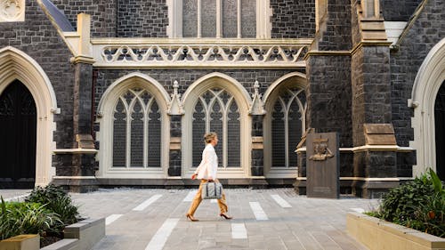 A photo of a person with a briefcase walking briskly past a historic bluestone church, recent paving and planter upgrades are seen in the foreground.