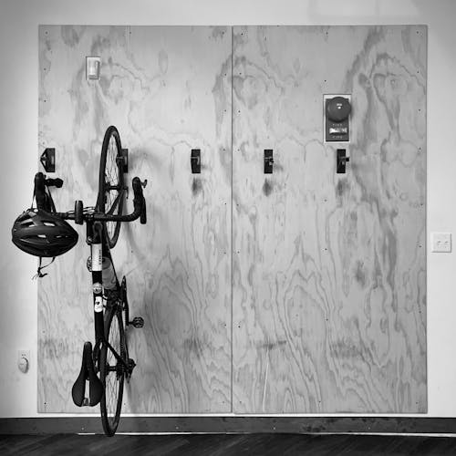 A black and white photograph of an indoor plywood bike rack. There is one bicycle hanging on the wall to the left of the image.