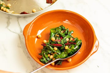 Chard and onions being arranged at the bottom of an oven-proof dish, with chickpeas scattered across the top.