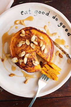 stack of pancakes served on plate garnished with maple syrup and butternut seeds