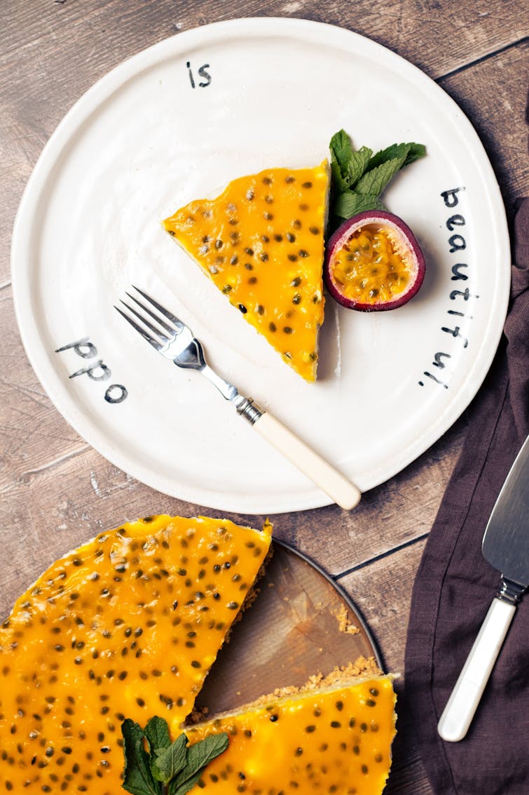 piece of vegan passion fruit cheesecake served with half a passionfruit and mint. On the side tray of vegan passionfruit cheesecake 