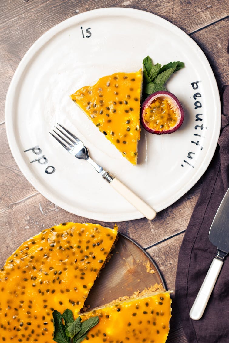 piece of vegan passion fruit cheesecake served with half a passionfruit and mint. On the side tray of vegan passionfruit cheesecake