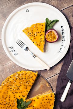 piece of vegan passion fruit cheesecake served with half a passionfruit and mint. On the side tray of vegan passionfruit cheesecake 