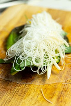The fillings of a Vietnamese summer roll. The first ingredient is herbs, then lettuce, vegetables, and everything is topped with a tablespoon of noodles. 