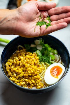 Seaweed flakes being added to a bowl of ramen.