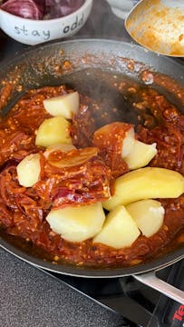 potatoes being tossed with Bombay sauce in a saucepan 