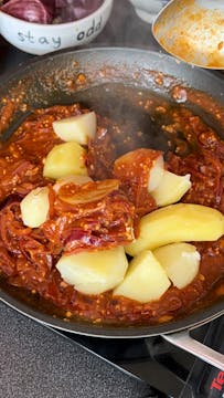 potatoes being tossed with Bombay sauce in a saucepan