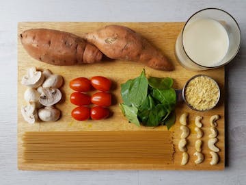 The ingredients required to make Creamy Sweet Potato Spaghetti with Roasted Veg. Sweet potato, milk (of choice), nutritional yeast, cashews, tomatoes, mushrooms, spaghetti, and spinach.