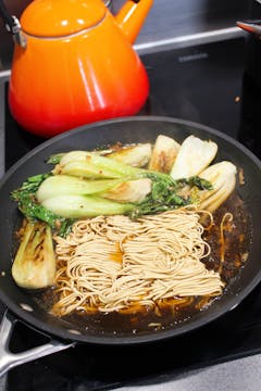 Noodles being cooked in the pan with the pak choi. 