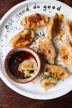 A plate of mushroom, cabbage, and potato potstickers with a bowl of dipping sauce. 