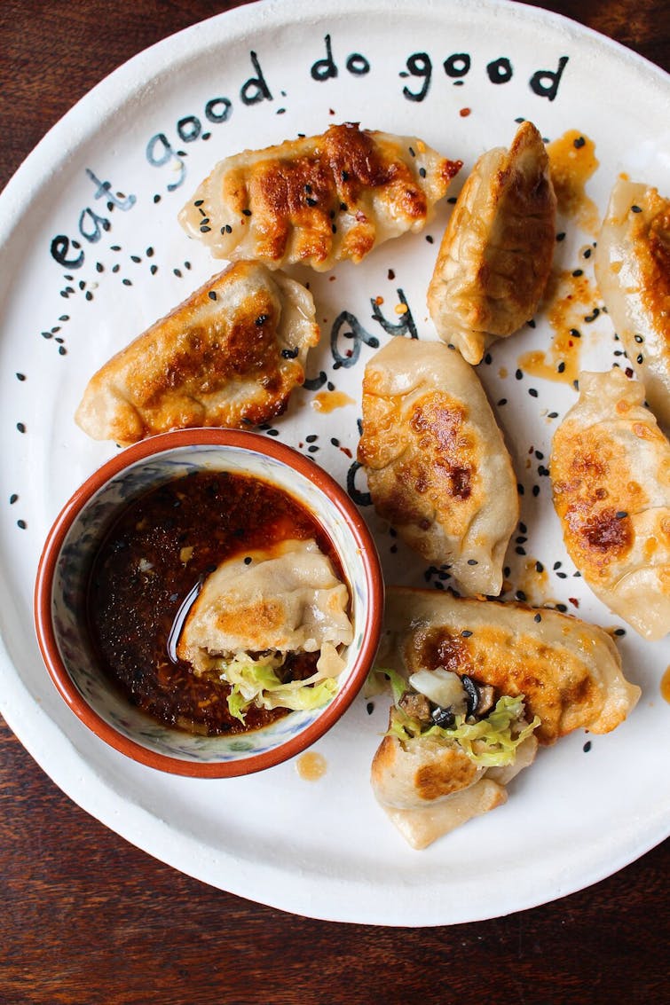 A plate of mushroom, cabbage, and potato potstickers with a bowl of dipping sauce. 