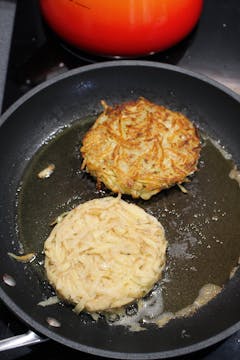 frying pan with 2 potato rosti being fried in oil