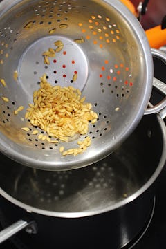 Melon seeds being poured from a sieve into a pot, ready to be cooked. 
