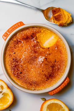 whole Seville Orange & Cardamom Crème Brûlée with orange slices next to the dish and spoon full of the Crème Brûlée on the side