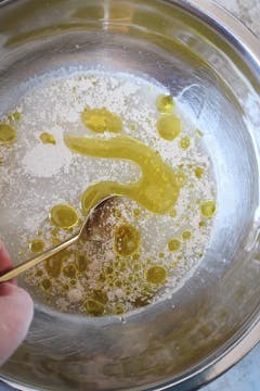 The wet and dry ingredients for the pizza dough being mixed with a spoon. 