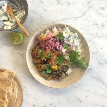 Aubergine, Peanut & Tamarind Curry with white rice, garnished with thinly sliced red onions and coriander leaves on a white bowl