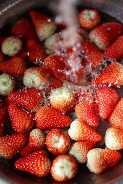 A pile of strawberries being washed in a bowl under water