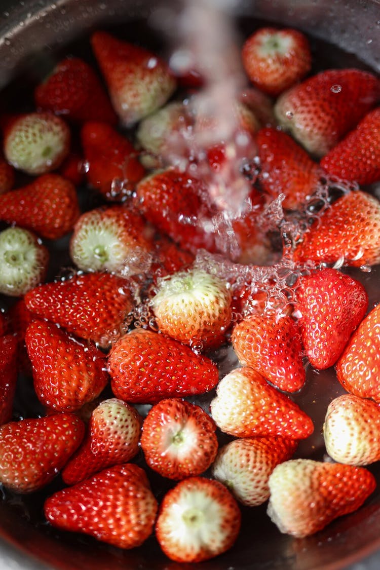 A pile of strawberries being washed in a bowl under water