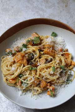 plate of sweet potato carbonara garnished with grated Parmesan, chopped parsley and black pepper.