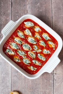 Stuffed pasta shells arranged in tomato sauce in an oven dish.