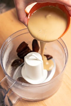 Whole dates, tahini, and maple syrup combined in a food processor.