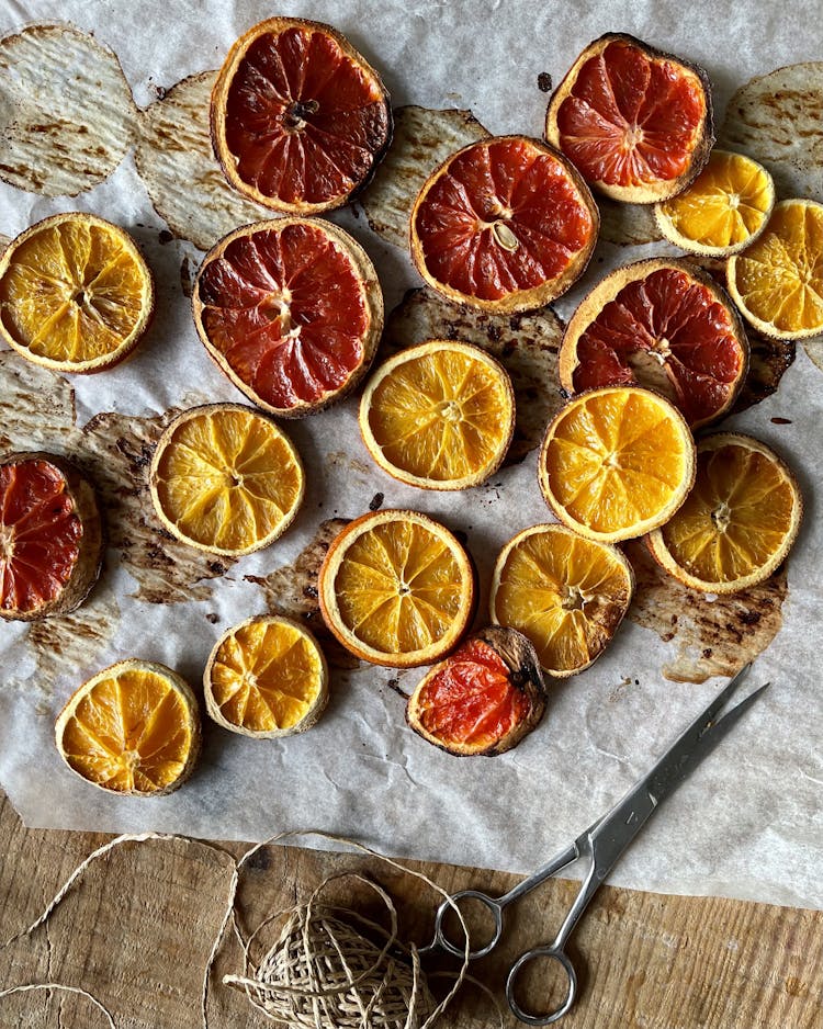 Dried oranges laid out on baking paper with string and scissors 