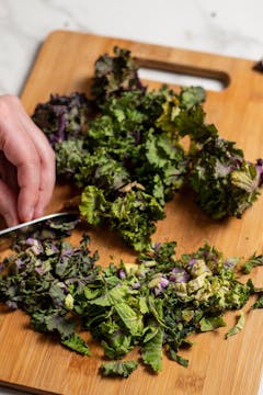 Bunch of fresh kalettes getting chopped on a wooden chopping board 