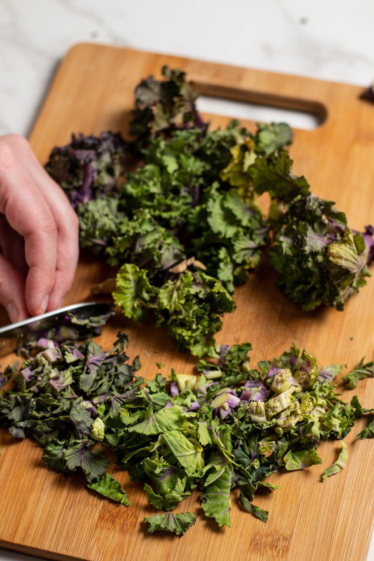 Bunch of fresh kalettes getting chopped on a wooden chopping board 
