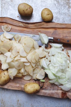 Finely sliced potatoes and onions on a chopping board. 