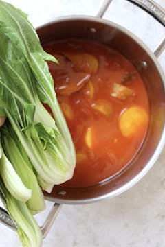 pak choi being added to the sauce pan