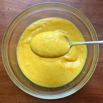 orange puree on a clear bowl and spoon full of puree up close 