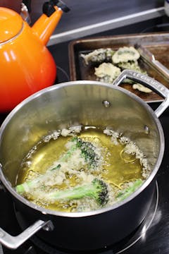 The battered sprouting broccoli being fried in a pot of vegetable oil. 