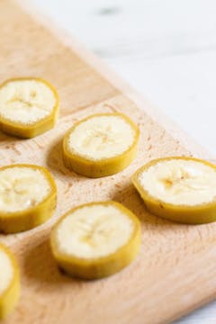 5 pieces of sliced banana still in the peel on a chopping board