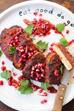 sticky pomegranate tofu steaks on a white plate with a knife