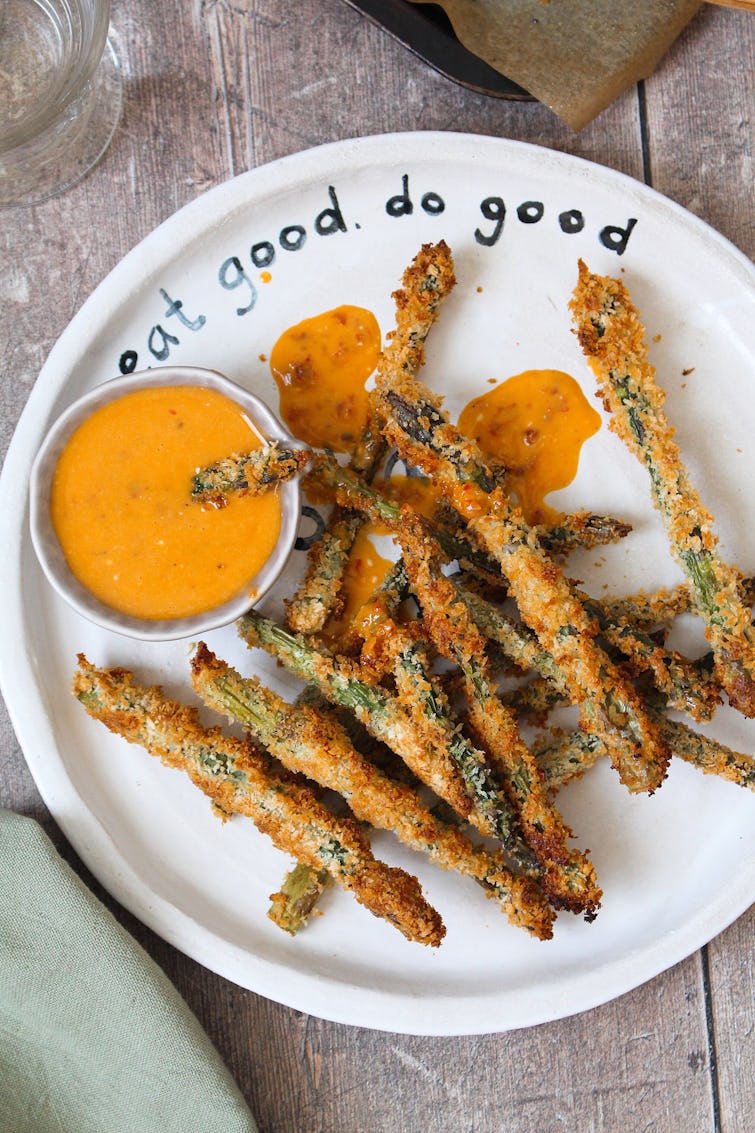 A plate of asparagus fries with a bowl of dipping sauce. 
