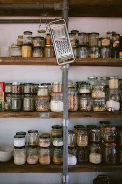 A grater hanging in front of 3 shelves full of jarred spices and other dried goods. 