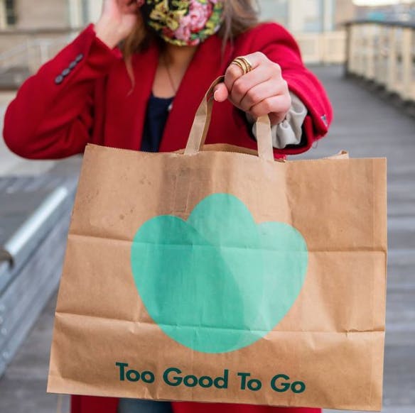 A woman in a face mask holding a paper Too Good to Go Bag