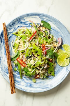 Herby Thai Noodle Salad with Charred Flat Beans on a plate, garnished with limes. There is a pair of chopsticks on the plate next to the salad.