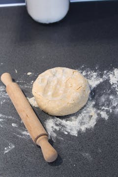 A rolling pin next to the kneaded dough on the floured worktop. 